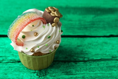 Image of St. Patrick's day. Tasty cupcake with sour rainbow belt and pot of gold toppers on green wooden table, closeup. Space for text