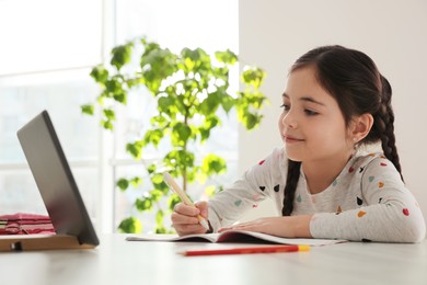 Little girl doing homework with modern tablet at home