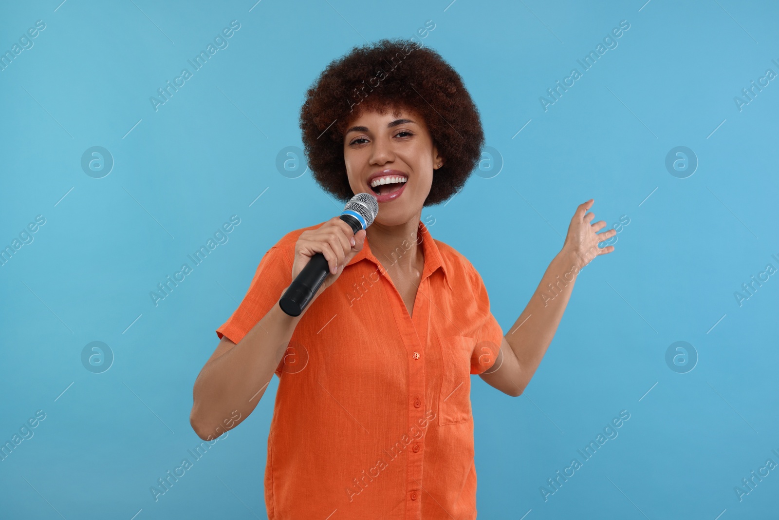 Photo of Curly young woman with microphone singing on light blue background