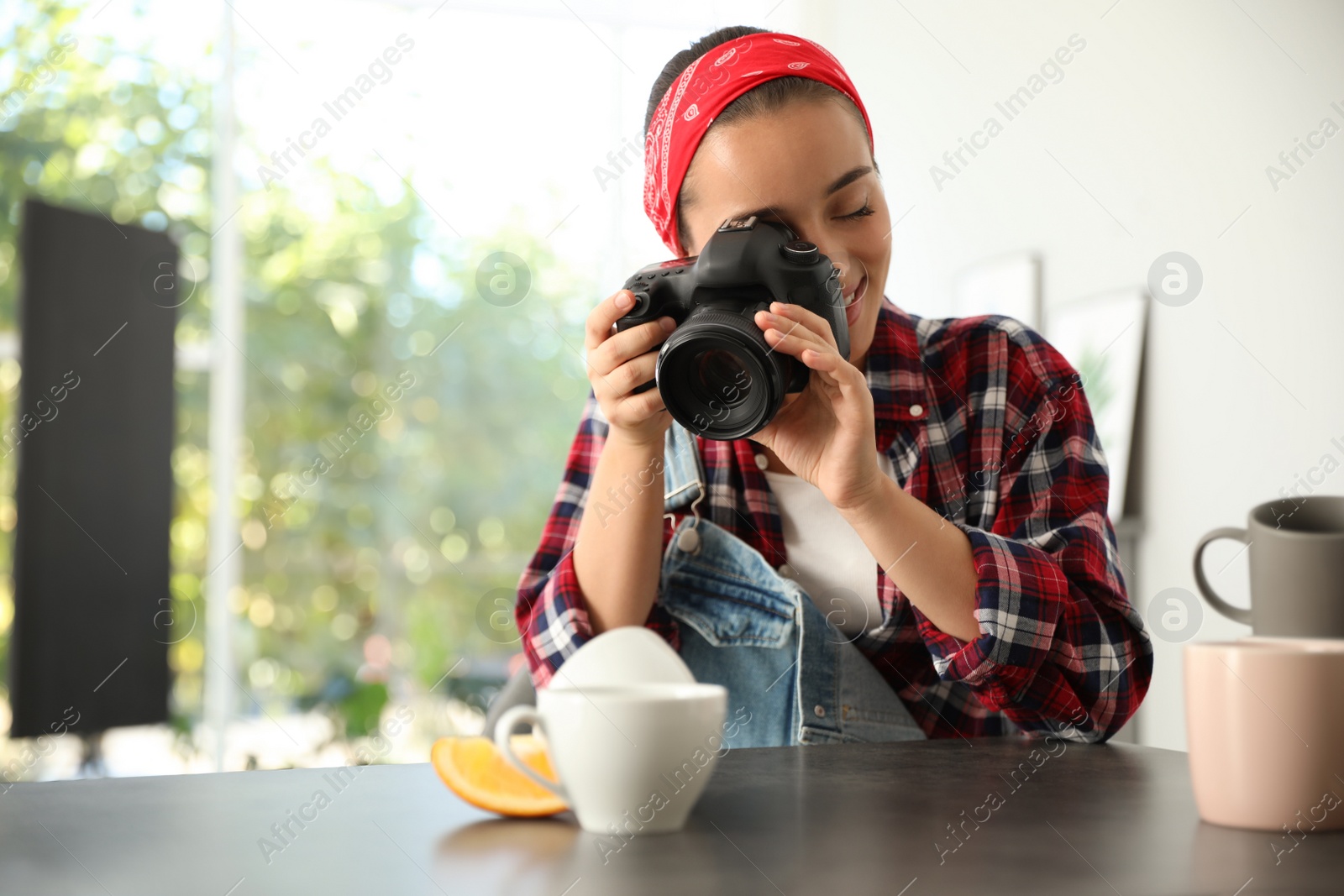 Photo of Young photographer taking picture of cups at table indoors