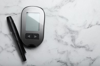 Photo of Glucometer and lancet pen on white marble table, flat lay with space for text. Diabetes testing kit