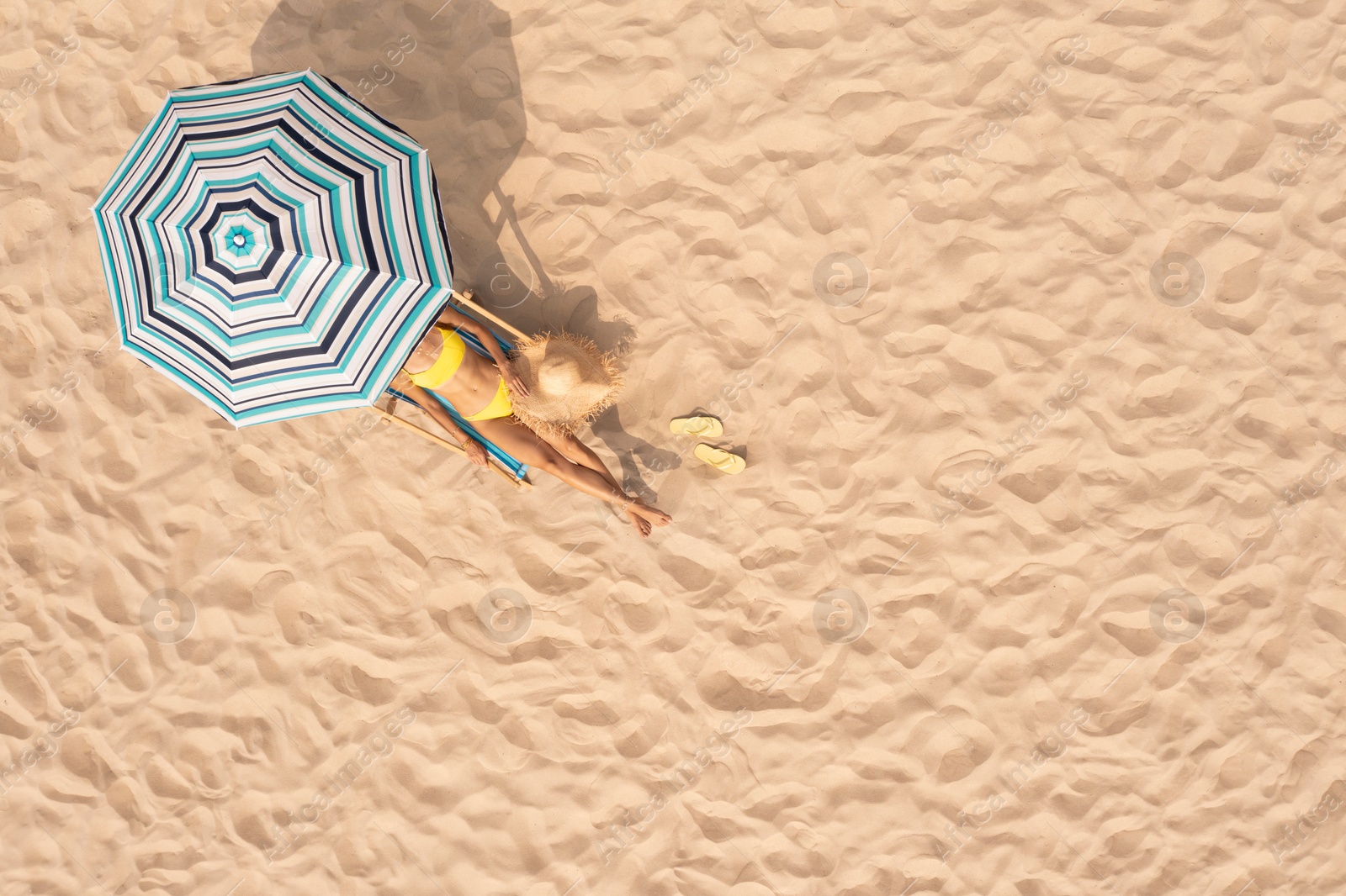 Image of Woman resting in sunbed under striped beach umbrella at sandy coast, aerial view. Space for text