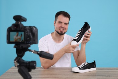 Photo of Smiling fashion blogger showing sneakers while recording video at table against light blue background