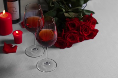 Romantic table setting with glasses of red wine, rose flowers and burning candles, space for text