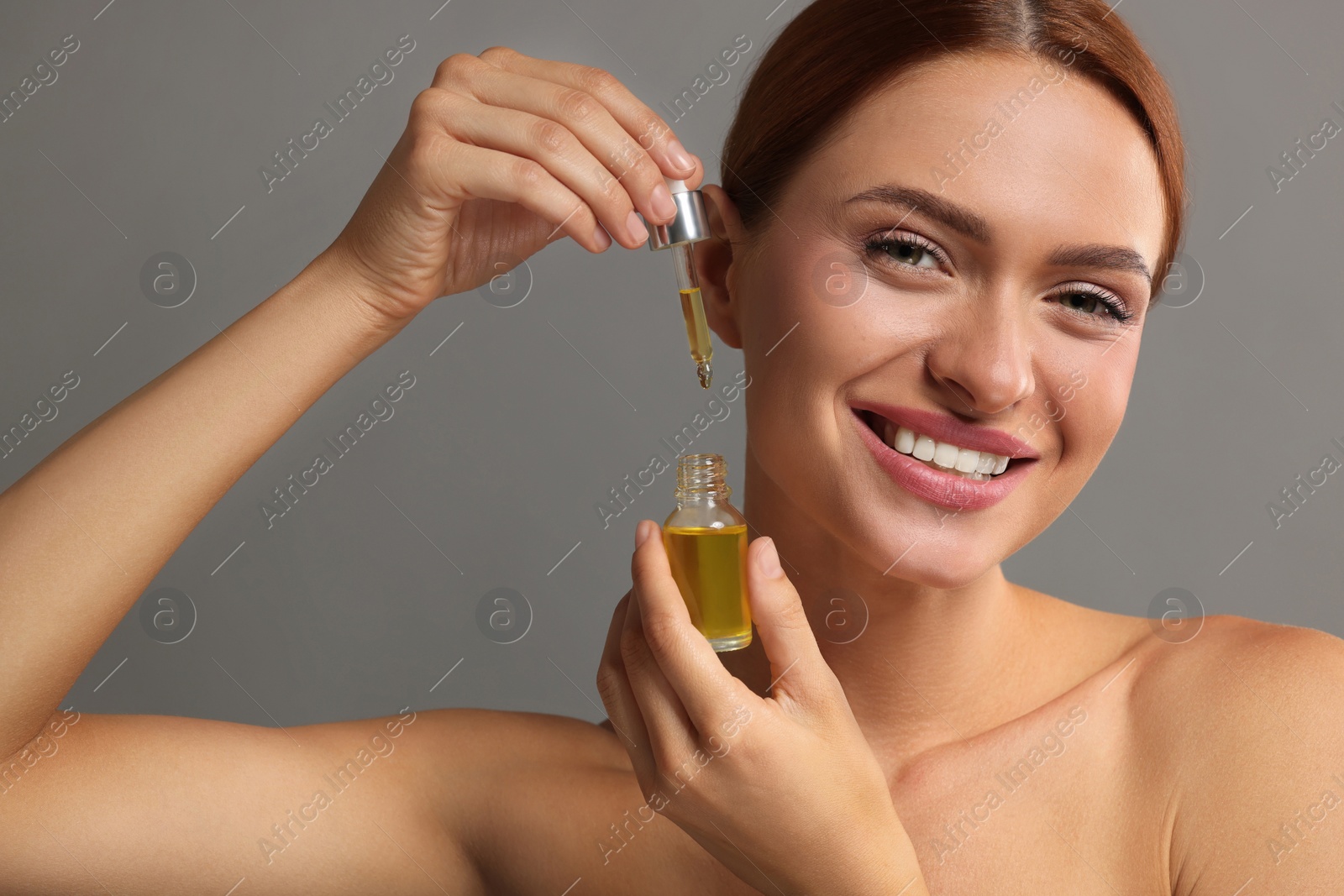 Photo of Beautiful young woman with bottle of cosmetic serum on grey background