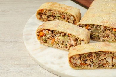 Photo of Cut tasty strudel with chicken and vegetables on light wooden table, closeup