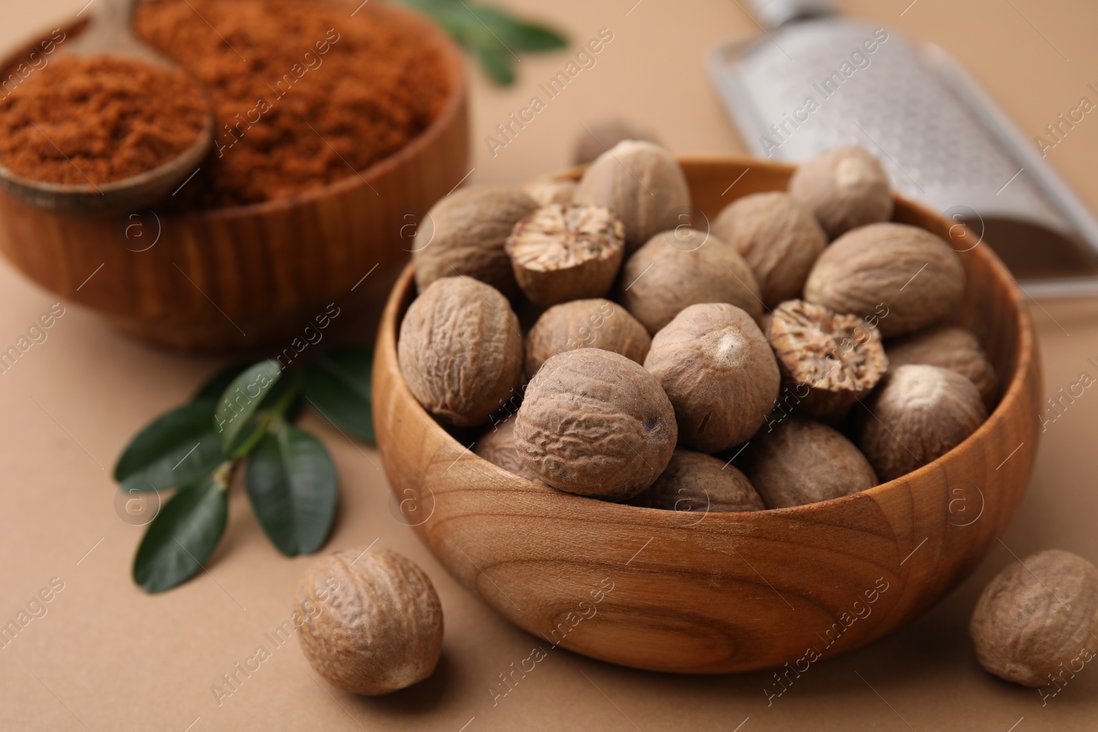 Photo of Nutmeg powder and seeds on light brown background, closeup