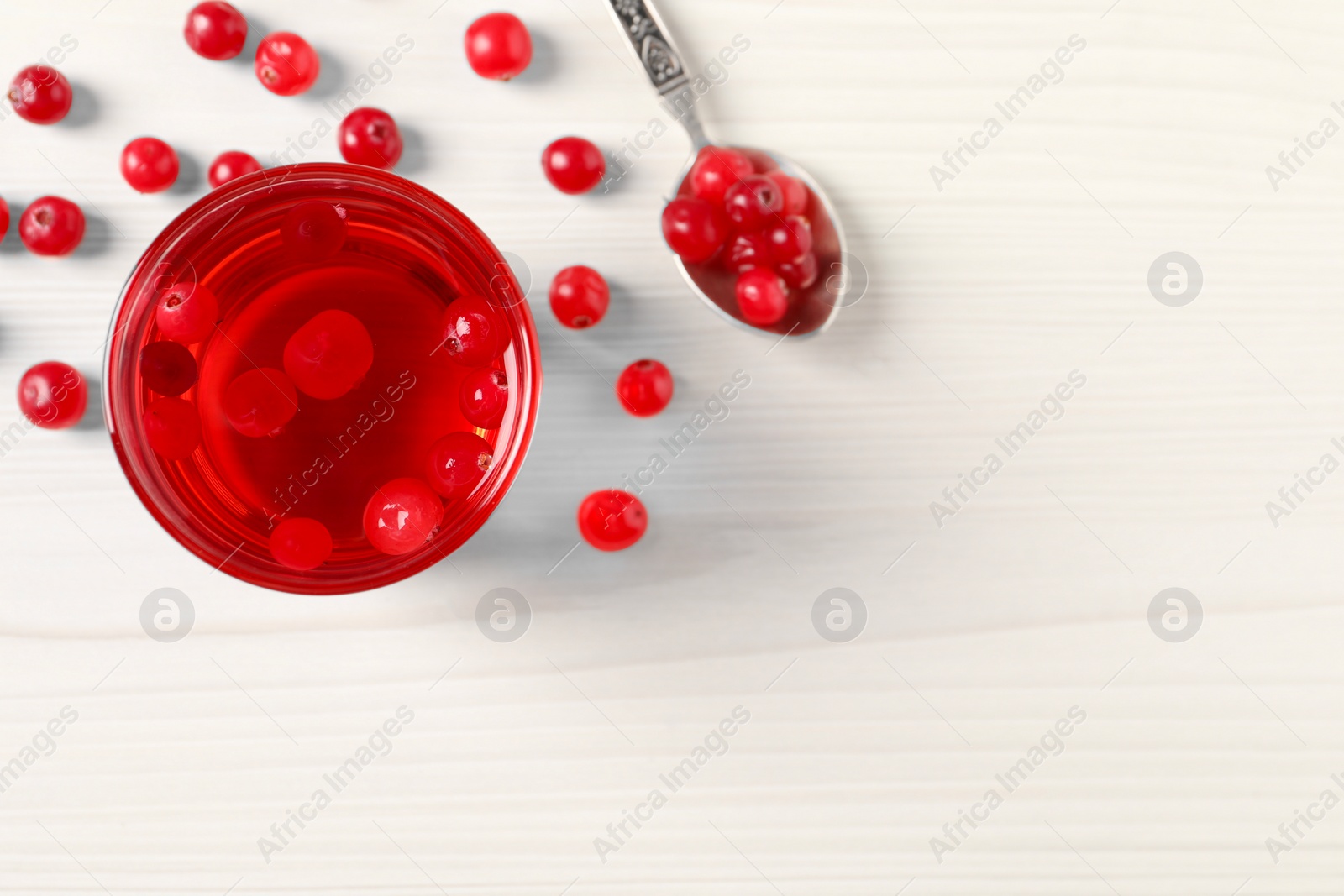 Photo of Tasty cranberry juice in glass and fresh berries on white wooden table, top view. Space for text