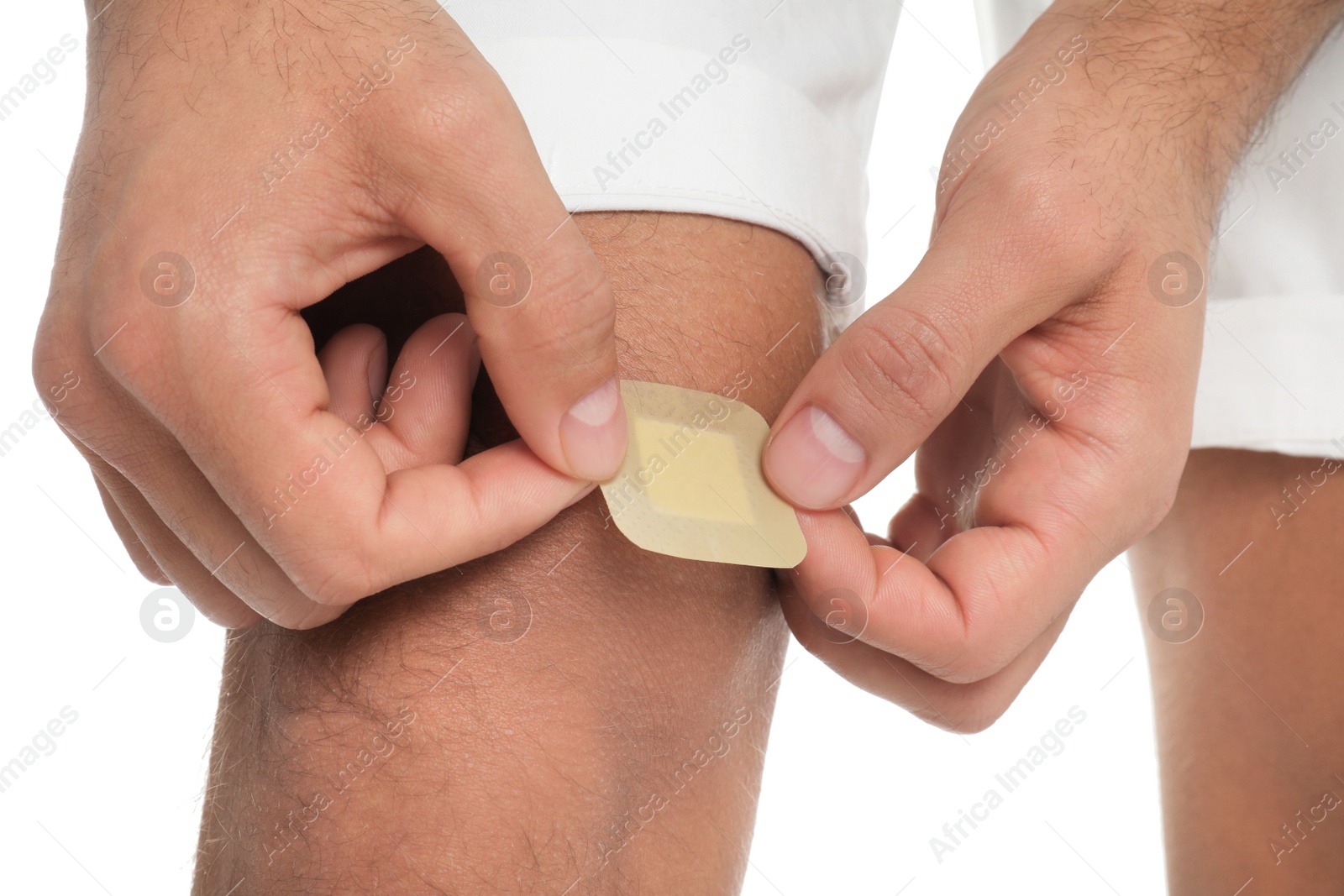 Photo of Man putting sticking plaster onto knee on white background, closeup