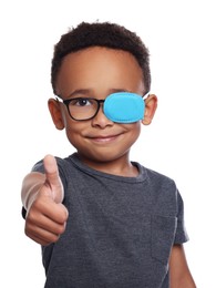 Photo of African American boy with eye patch on glasses showing thumb up against white background. Strabismus treatment