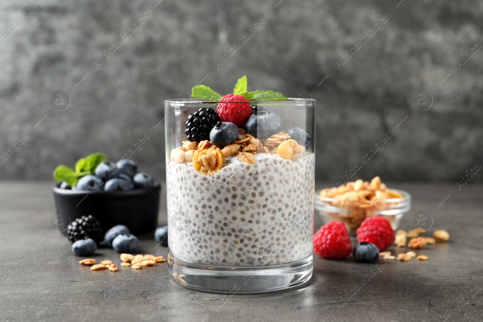 Photo of Delicious chia pudding with berries, granola and mint on grey table