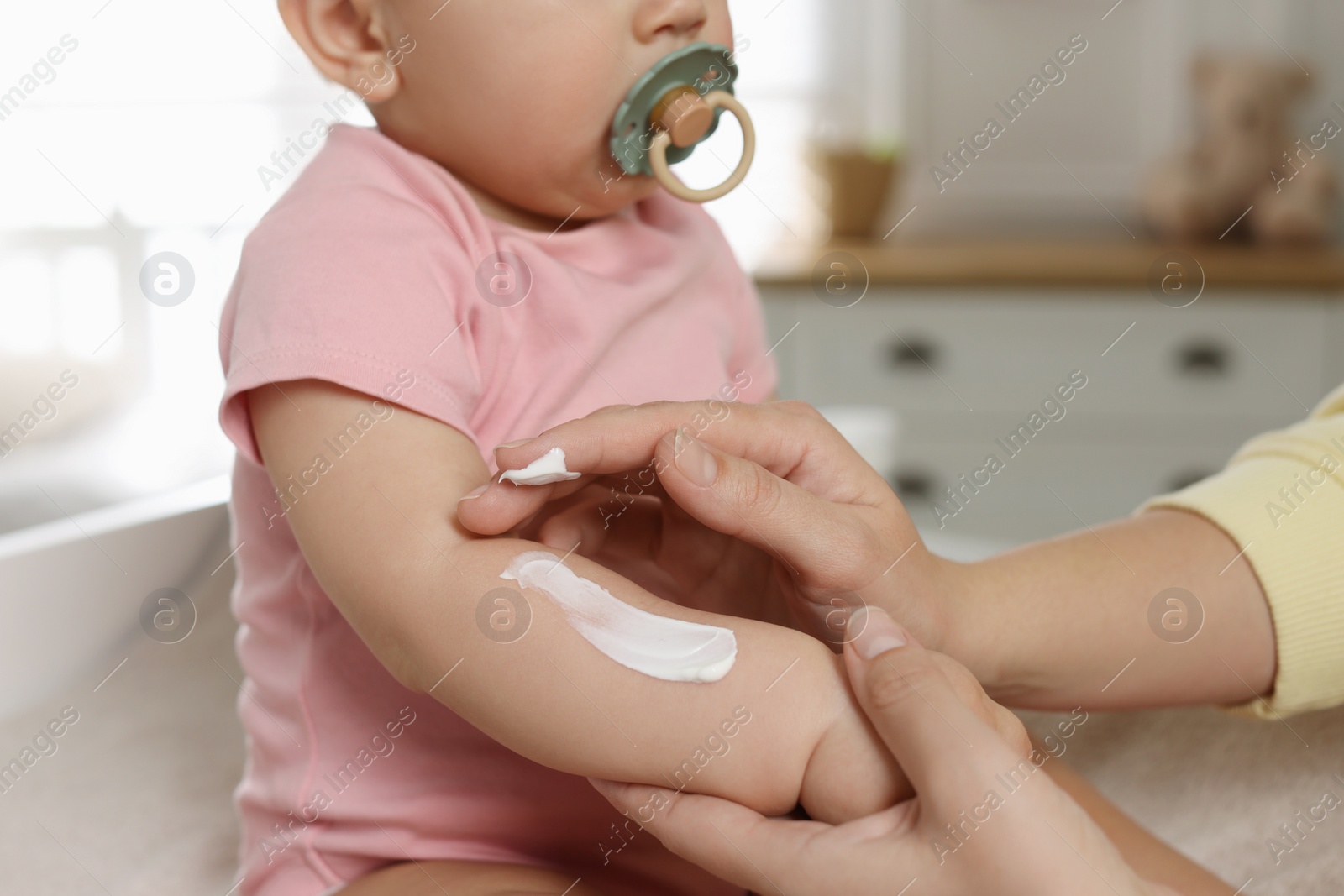 Photo of Mother applying body cream on her little baby at home, closeup