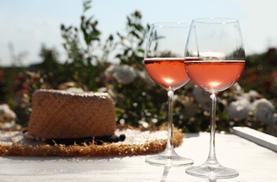 Photo of Glasses of rose wine and straw hat on white wooden table outdoors. Space for text
