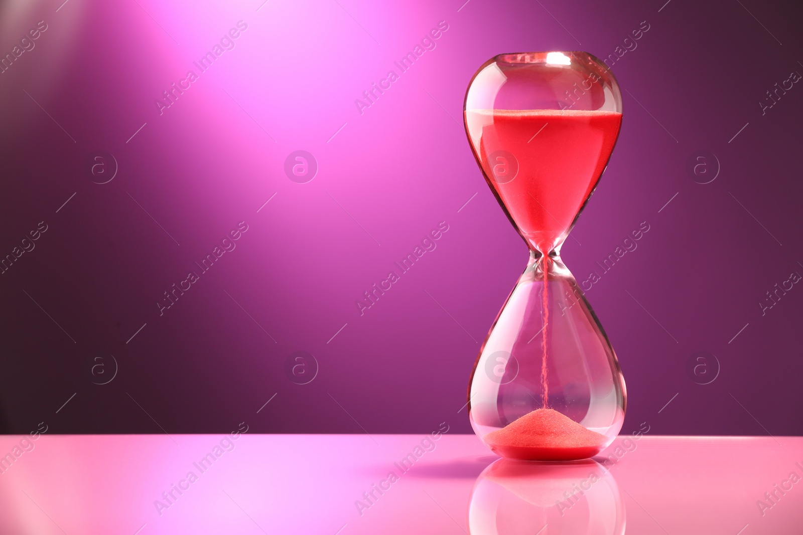 Photo of Hourglass with red flowing sand on color background, space for text