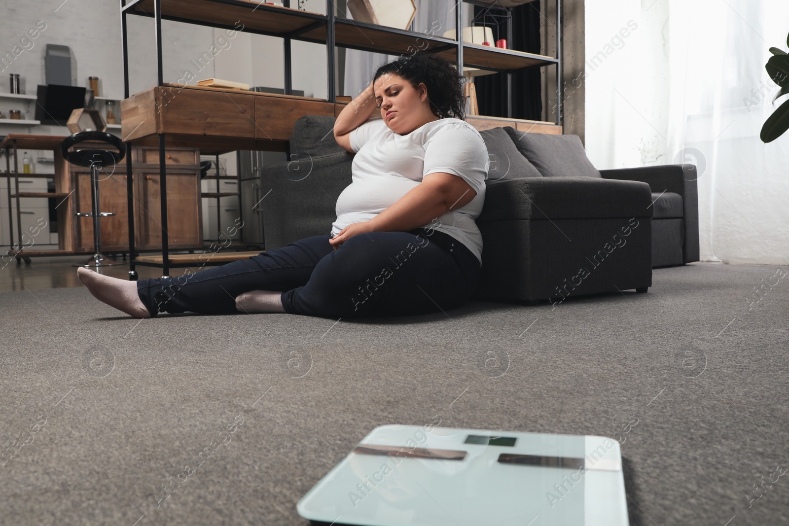 Photo of Scales and depressed overweight woman on floor at home