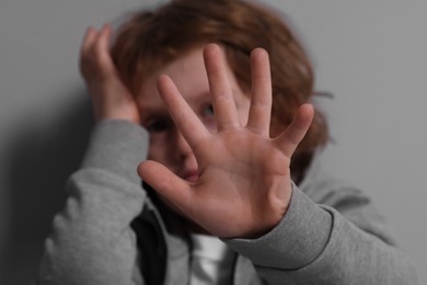 Photo of Child abuse. Boy making stop gesture near grey wall, selective focus