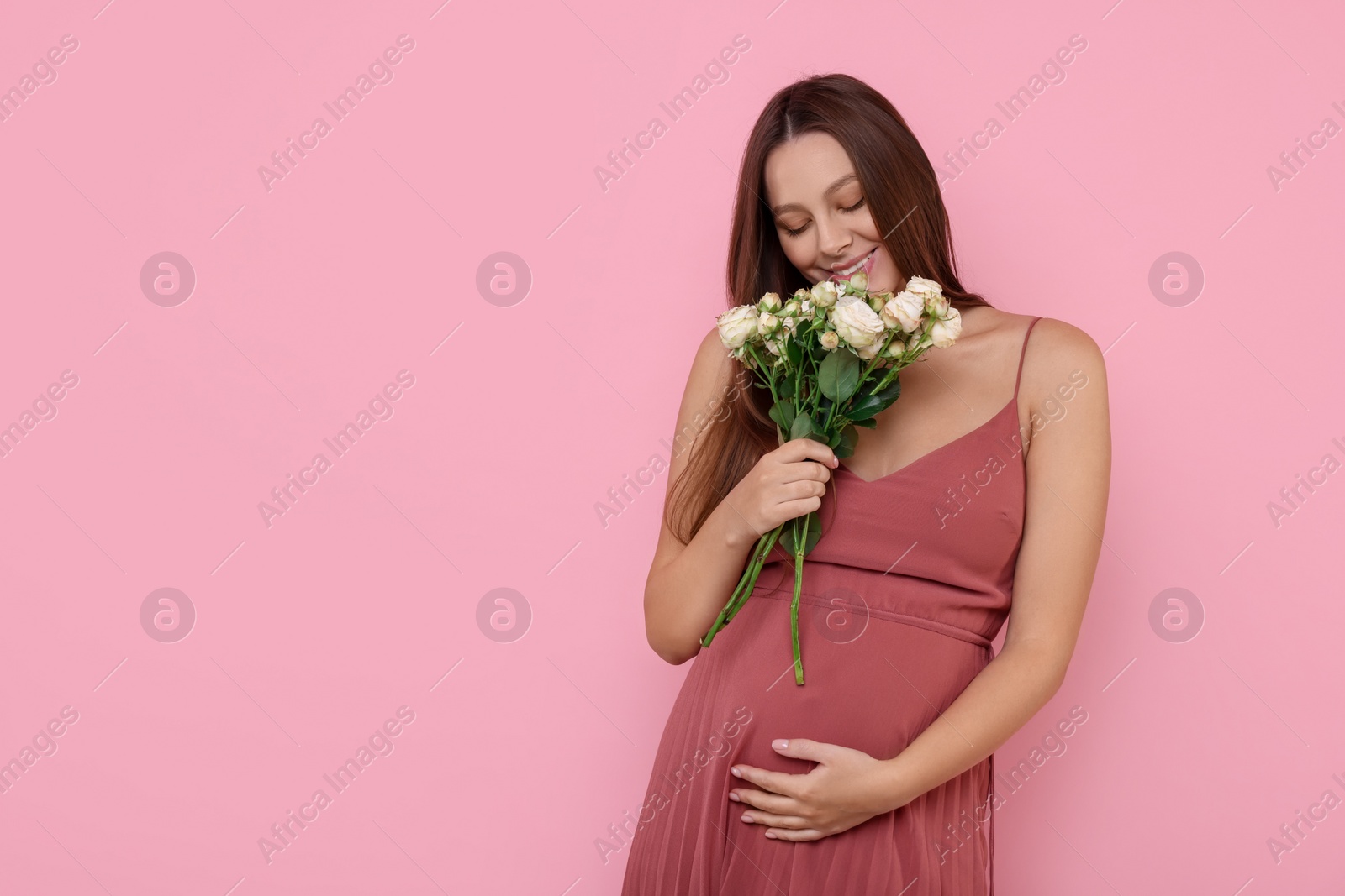 Photo of Beautiful pregnant woman in dress with bouquet of roses on pink background, space for text