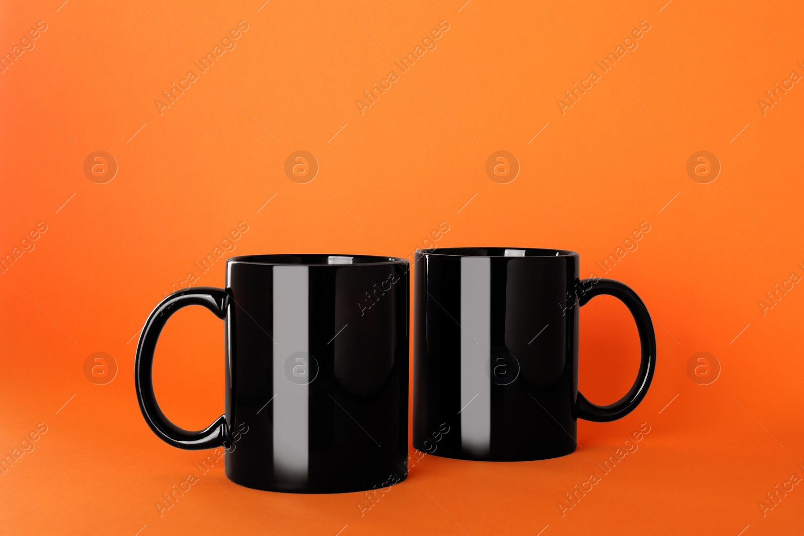 Blank black ceramic mugs on orange background Photo of Blank black ceramic mugs on orange background