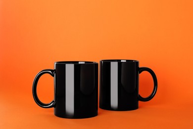 Photo of Blank black ceramic mugs on orange background