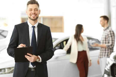 Photo of Salesman with clipboard and couple in salon. Buying new car