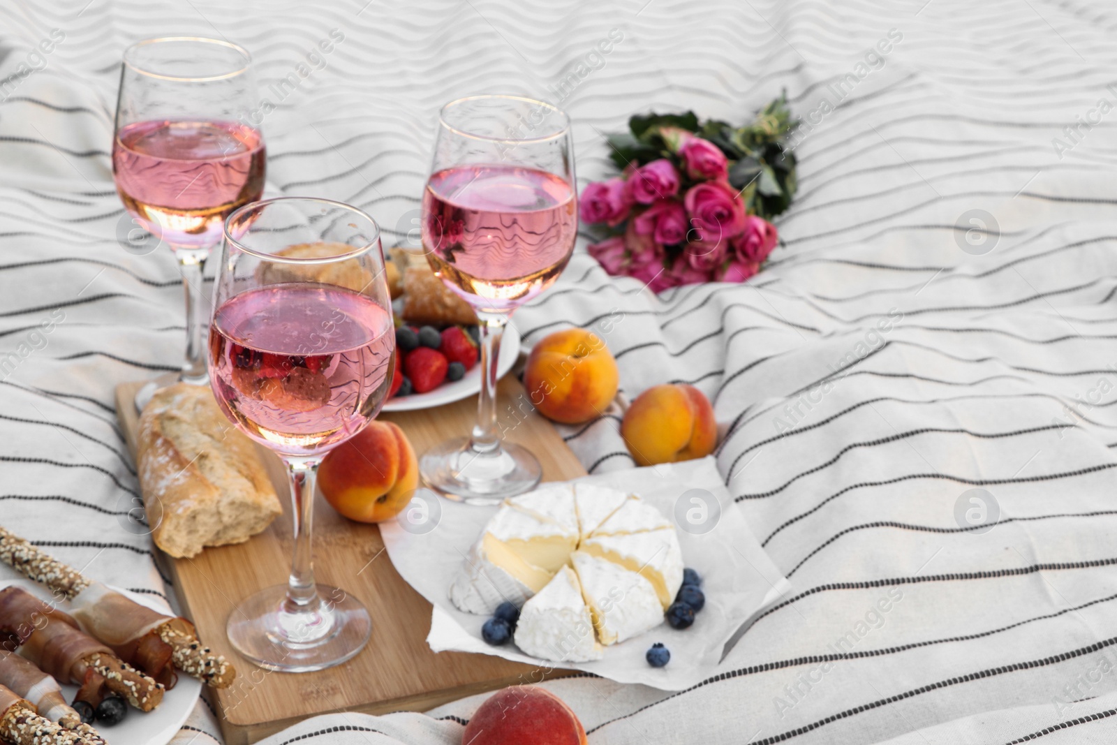 Photo of Glasses of delicious rose wine, flowers and food on white picnic blanket