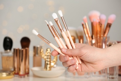 Woman holding makeup brushes over dressing table, closeup