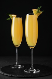 Photo of Glasses of Mimosa cocktail with garnish on black table