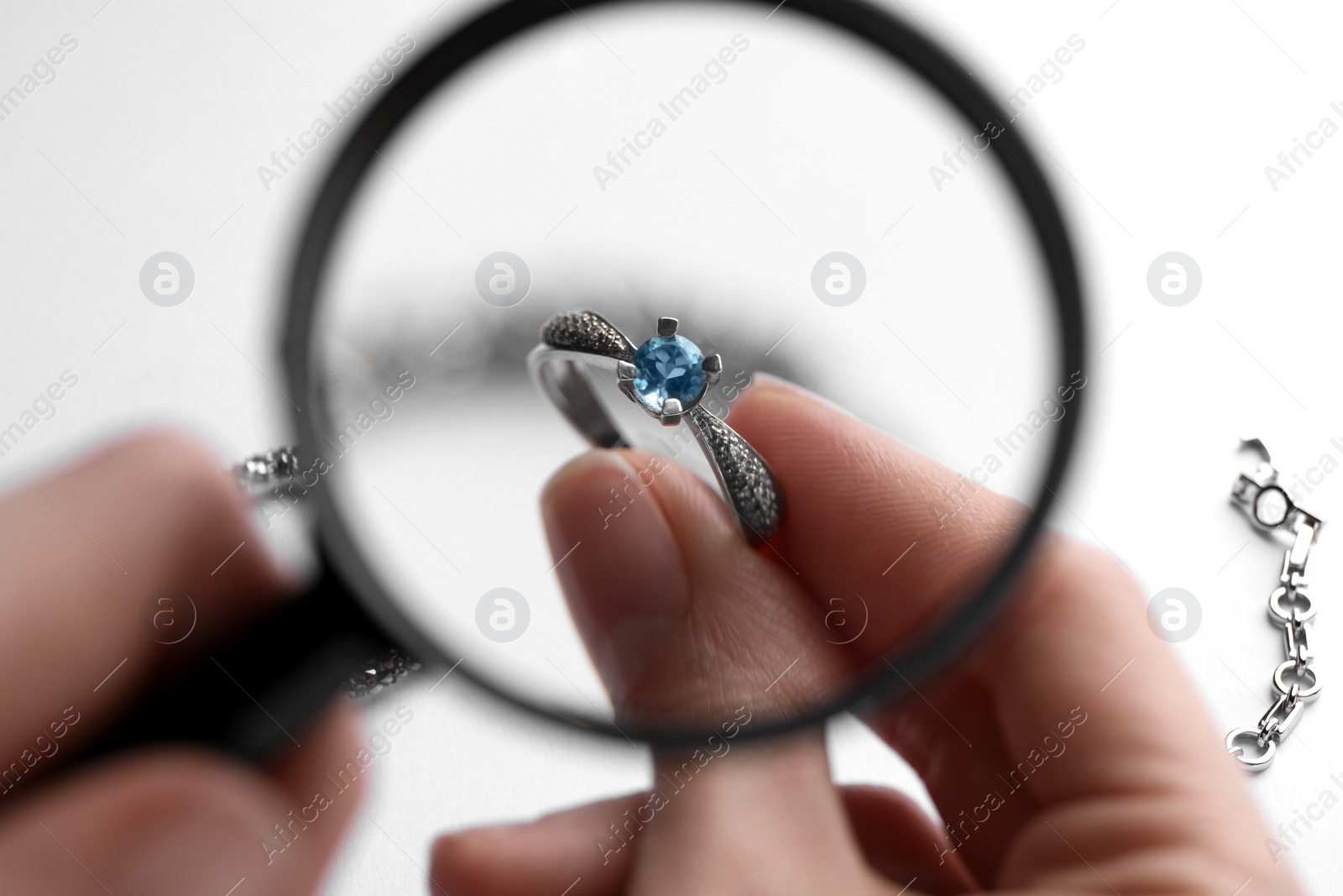 Photo of Jeweler examining topaz ring with magnifying glass at white table, closeup