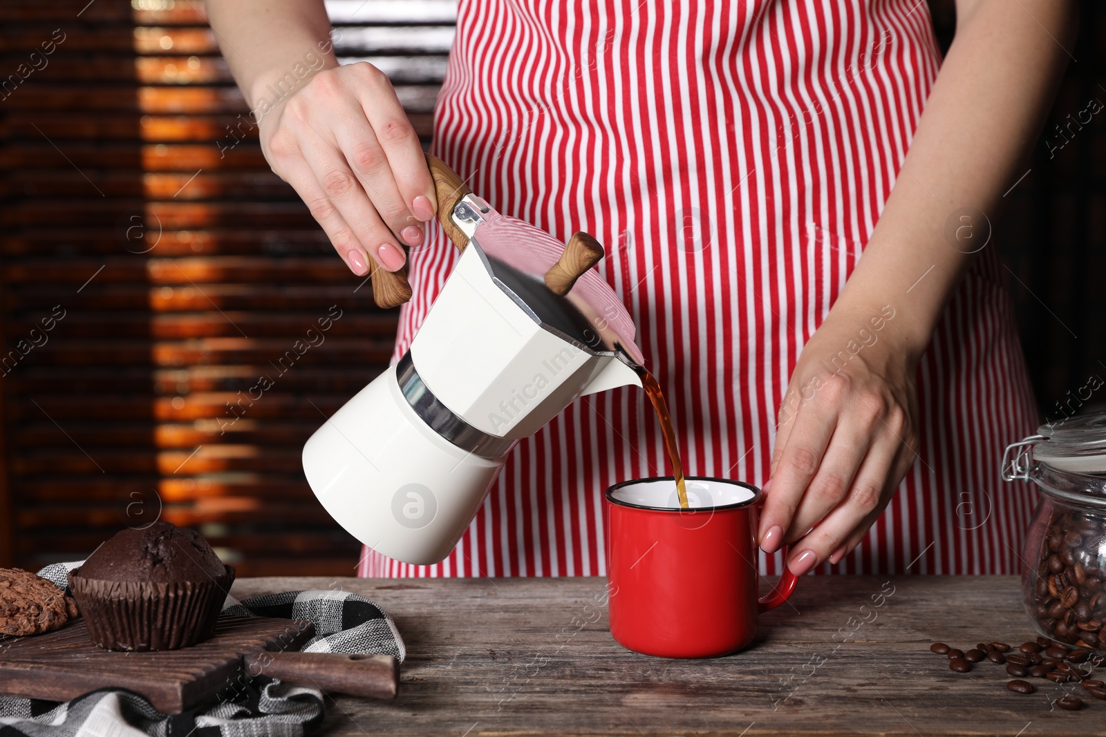 Photo of Woman pouring aromatic coffee from moka pot into cup at wooden table indoors, closeup