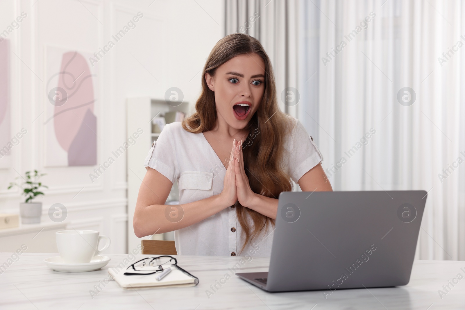 Photo of Surprised woman using laptop at white table in room