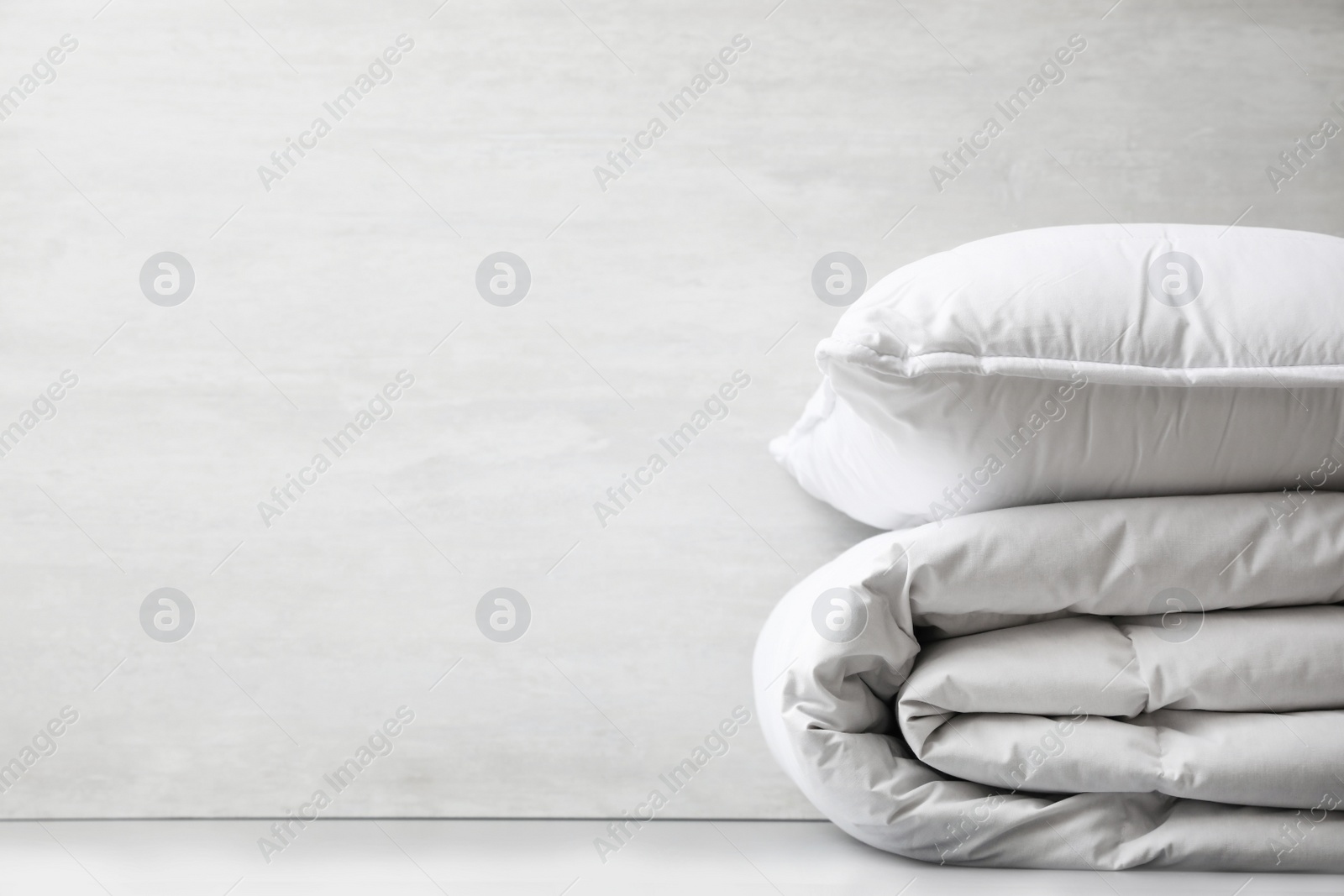 Photo of Soft folded blanket and pillow on light grey table, closeup. Space for text