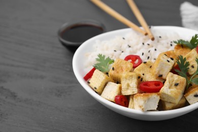 Photo of Bowl of rice with fried tofu, chili pepper and parsley on grey wooden table, closeup. Space for text