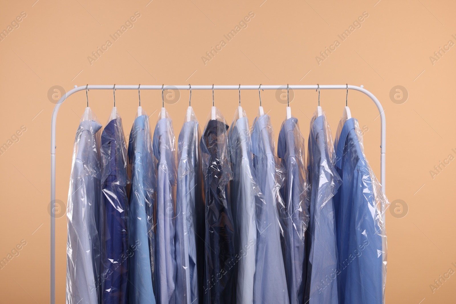 Photo of Dry-cleaning service. Many different clothes in plastic bags hanging on rack against beige background