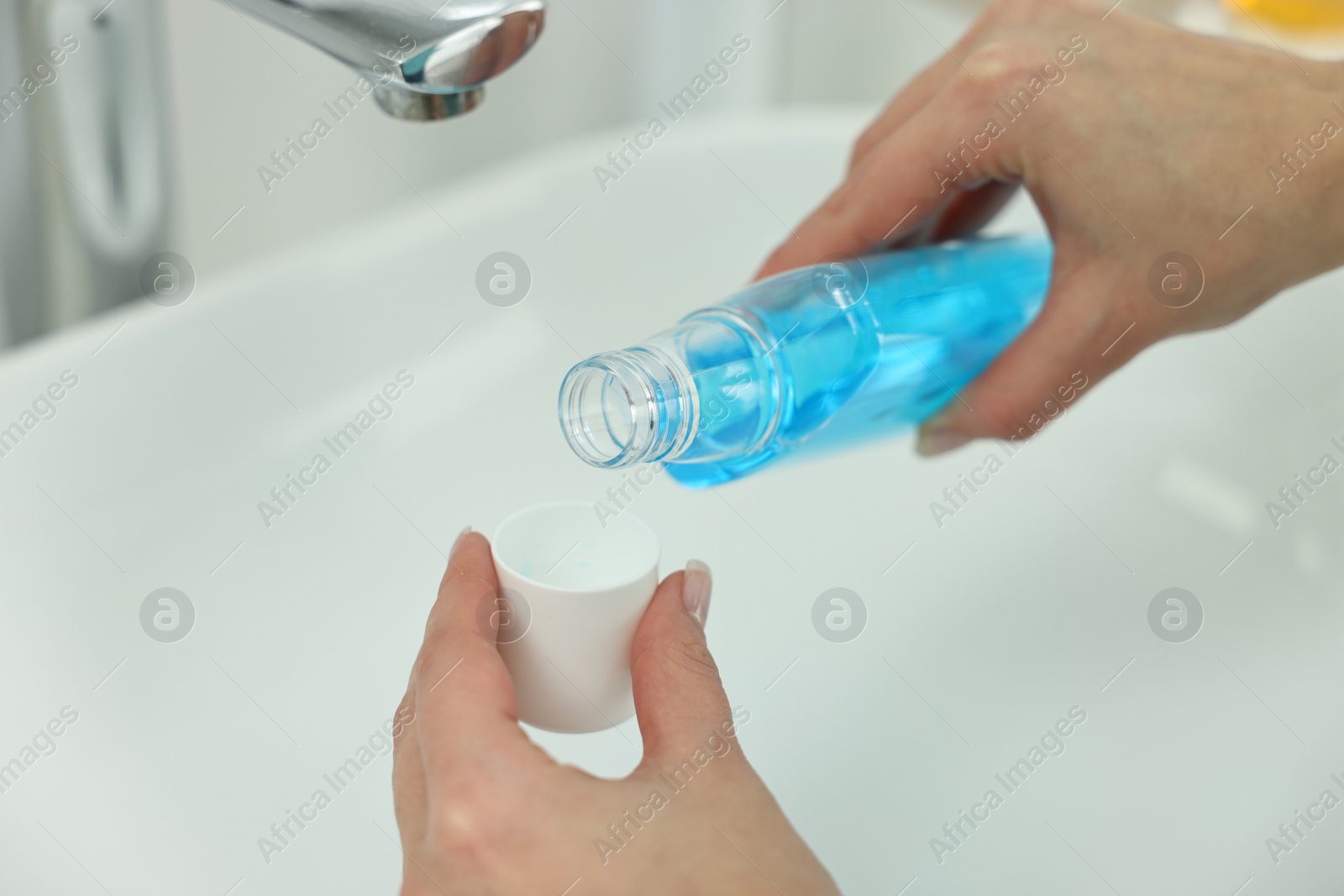 Photo of Young woman using mouthwash above sink in bathroom, closeup