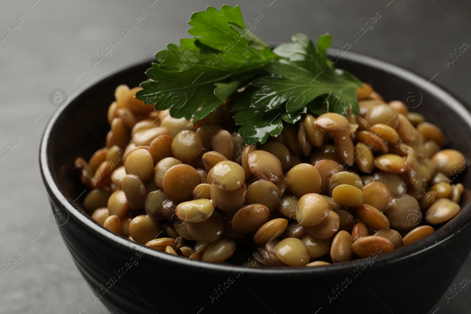 Photo of Delicious lentils with parsley in bowl on grey table, closeup