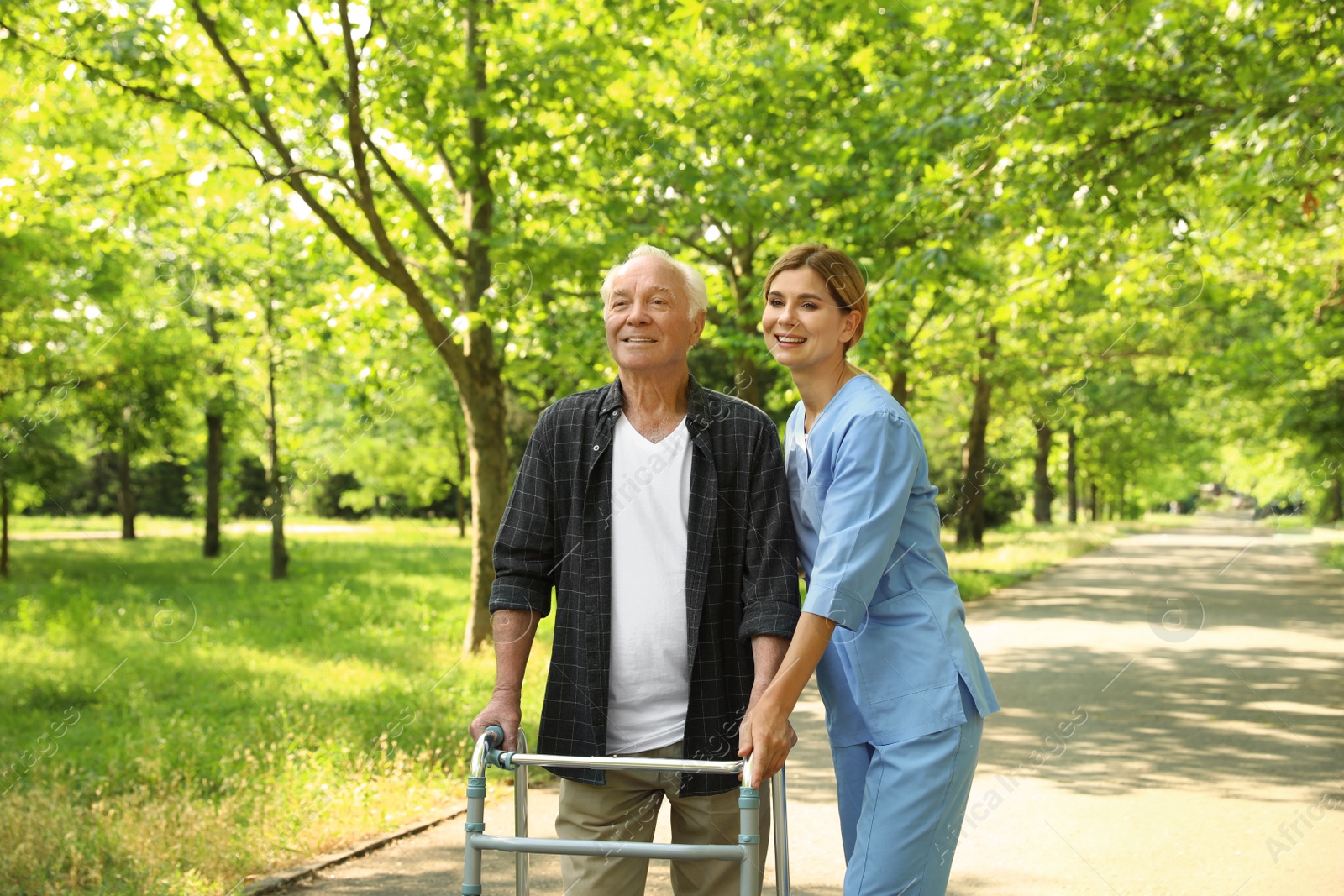 Photo of Happy nurse assisting elderly man with walking frame at park