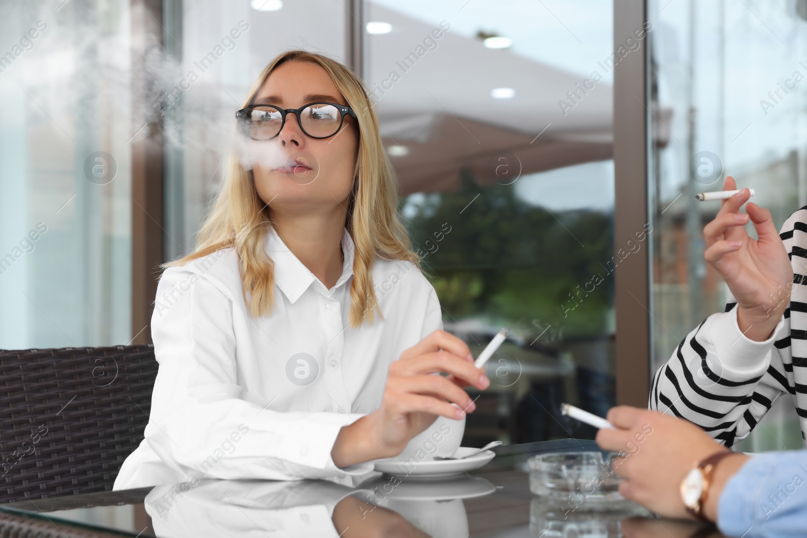 Photo of Women smoking cigarette at table in outdoor cafe