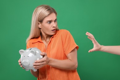 Scammer taking piggy bank from scared woman on green background. Be careful - fraud