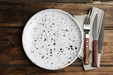 Photo of Empty patterned plate with cutlery and napkin on wooden table, flat lay