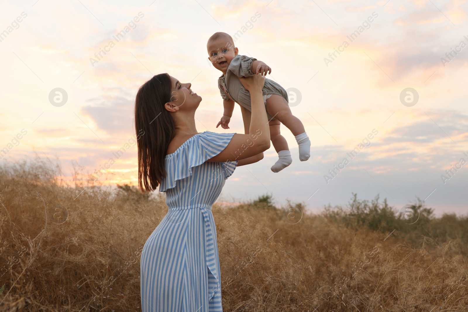 Photo of Happy mother with adorable baby in field at sunset