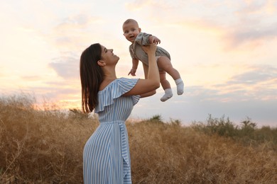 Happy mother with adorable baby in field at sunset