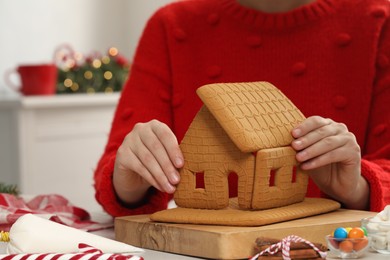 Photo of Woman in red sweater making gingerbread house indoors, closeup