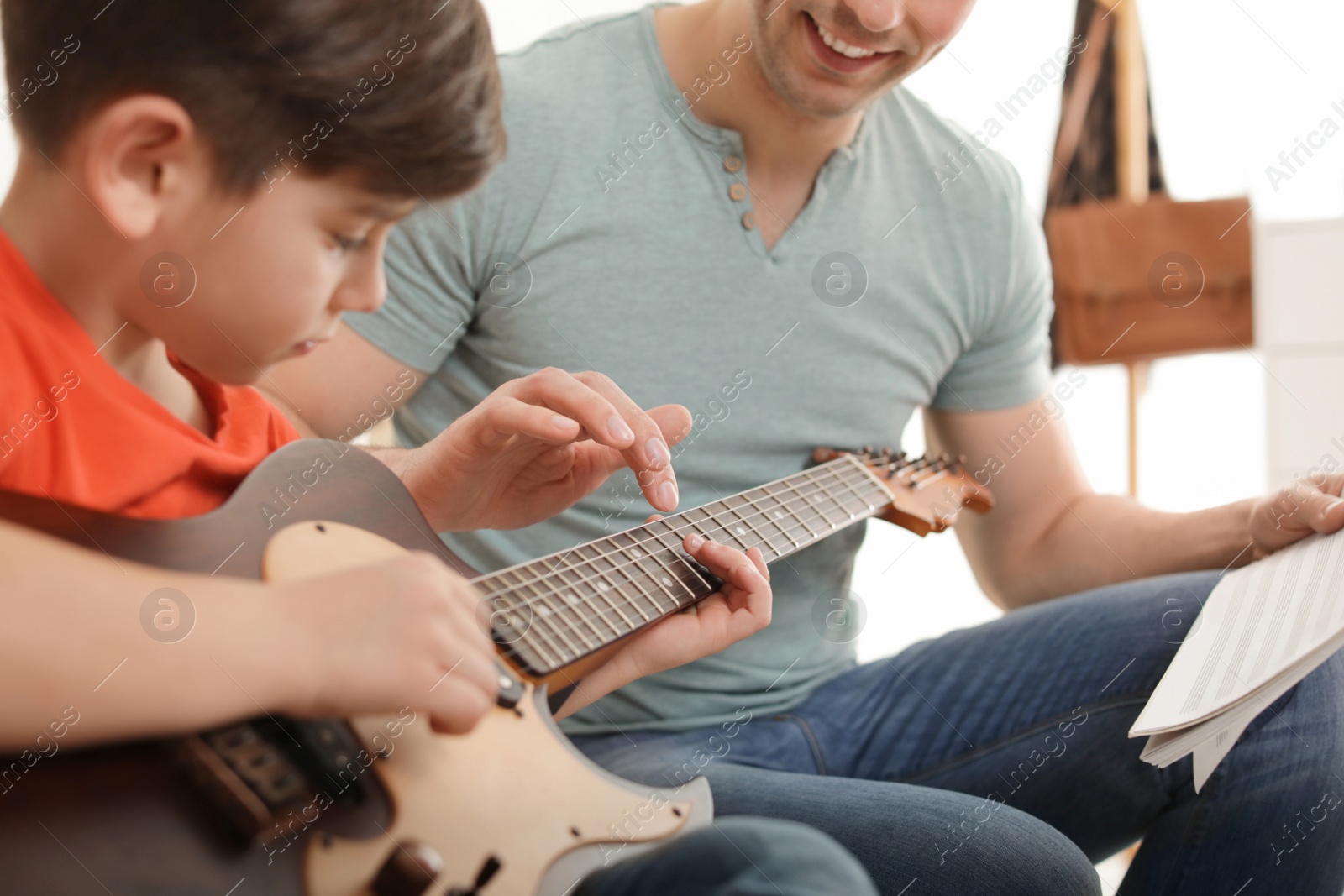 Photo of Little boy playing guitar with his teacher at music lesson, closeup. Learning notes