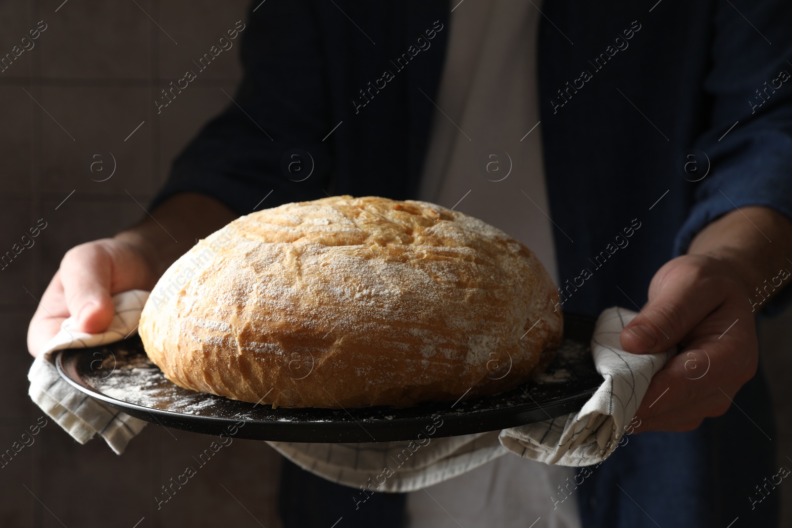 Photo of Man holding loaf of fresh bread on dark background, closeup