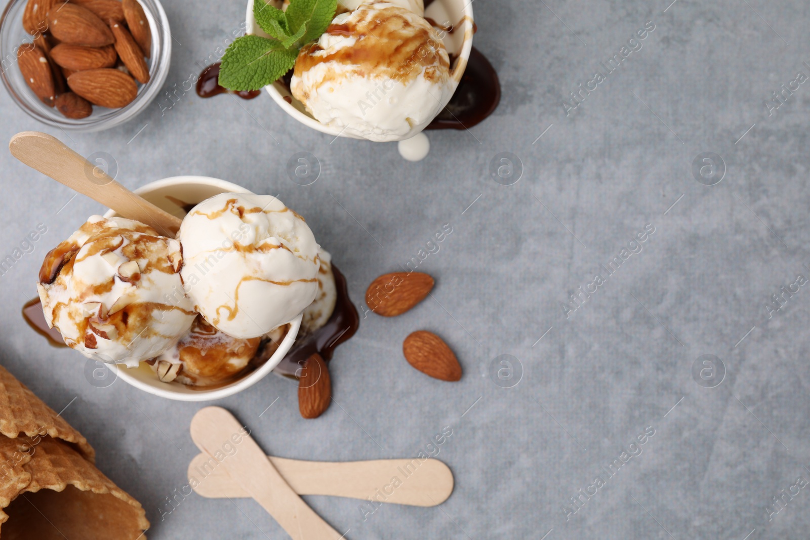 Photo of Scoops of ice cream with caramel sauce and nuts on light grey table, flat lay. Space for text