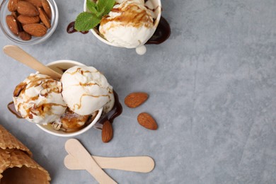 Scoops of ice cream with caramel sauce and nuts on light grey table, flat lay. Space for text