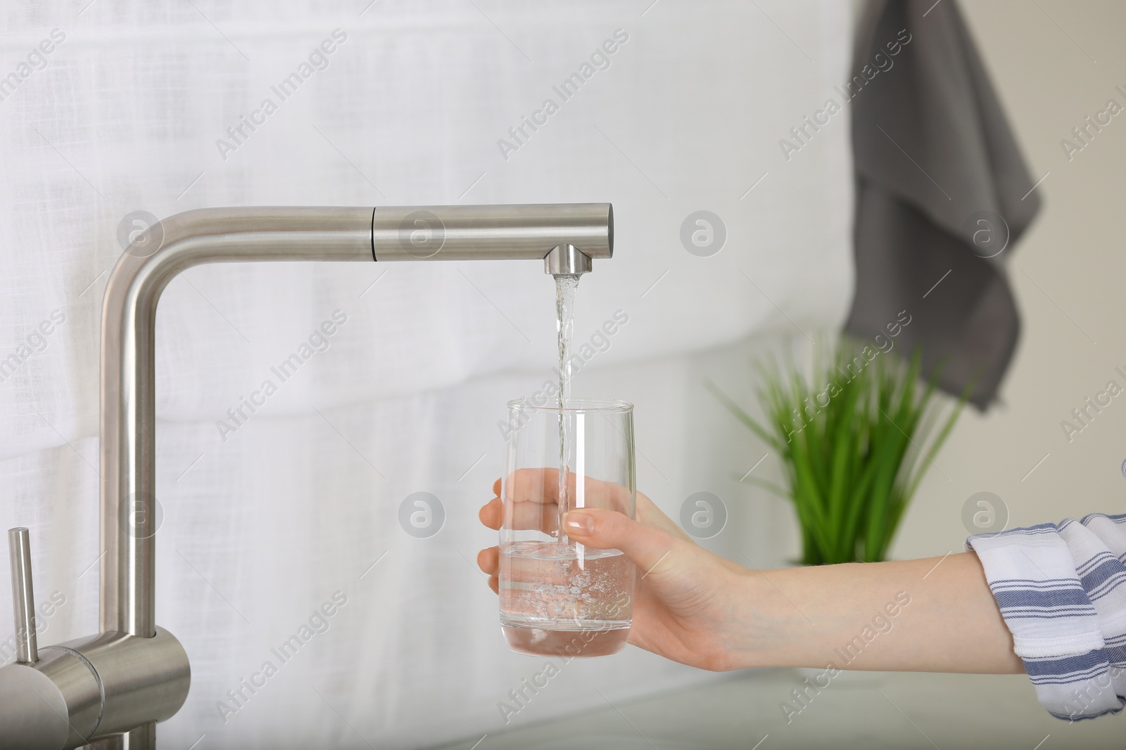 Photo of Woman filling glass with tap water from faucet in kitchen, closeup