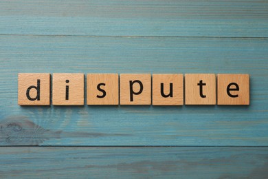 Squares with word Dispute on light blue wooden table, top view