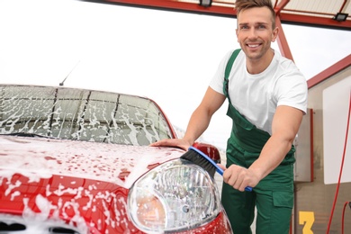 Male worker cleaning vehicle with brush at car wash