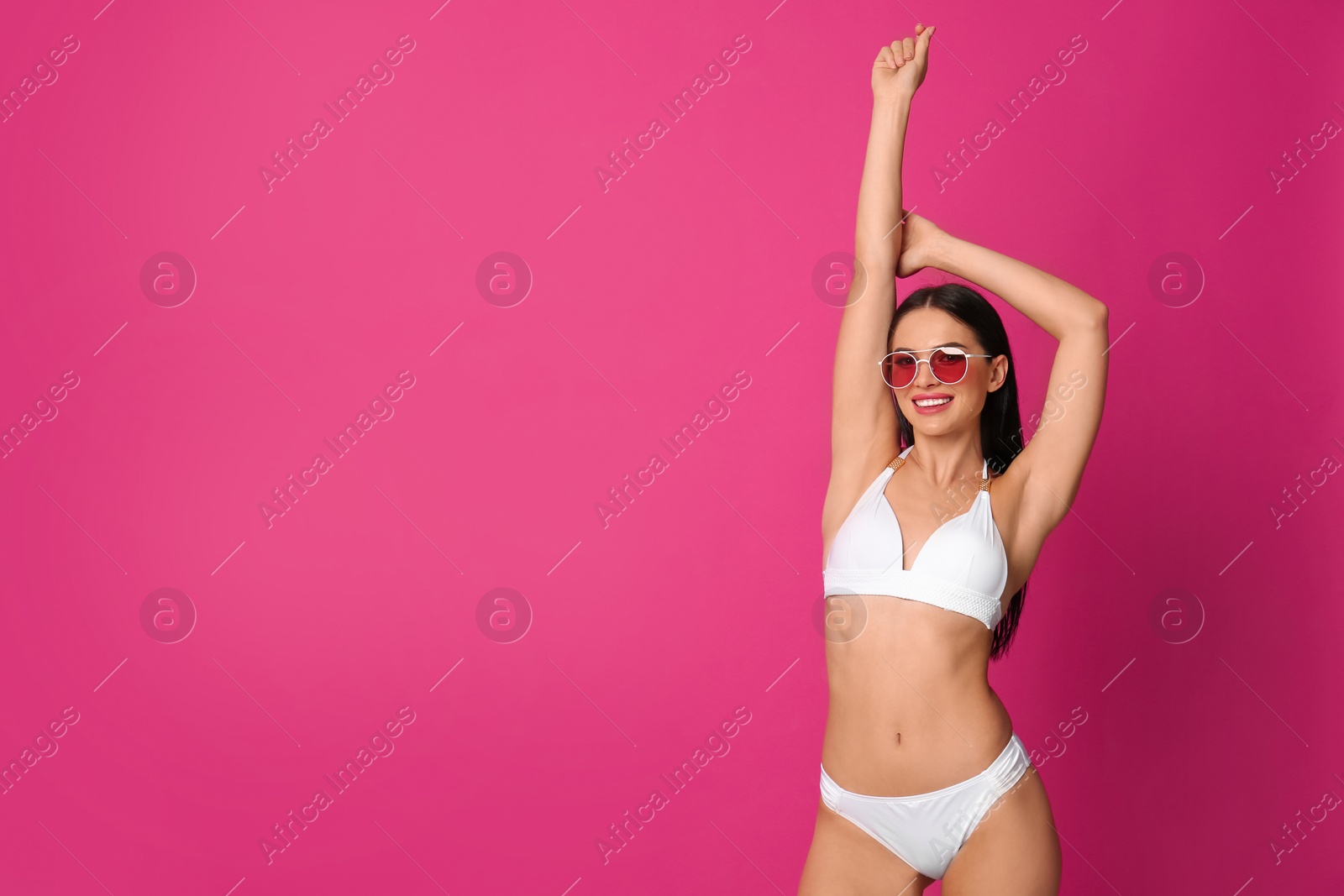 Photo of Beautiful young woman in white bikini with sunglasses on pink background. Space for text